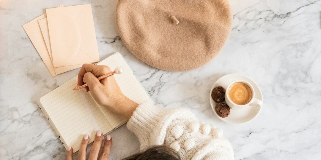 selected-01-person-writing-journal-morning-coffee-optimized Person skriver i en anteckningsbok med kaffe och basker på bordet